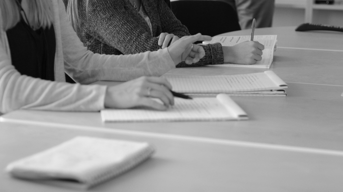 photo en noir et blanc de personnes en réunion, écrivant sur un cahier
