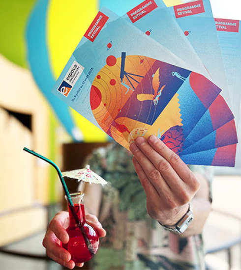 personne tendant devant lui les flyer de l'été et un ballon rempli d'eau coloré en rouge