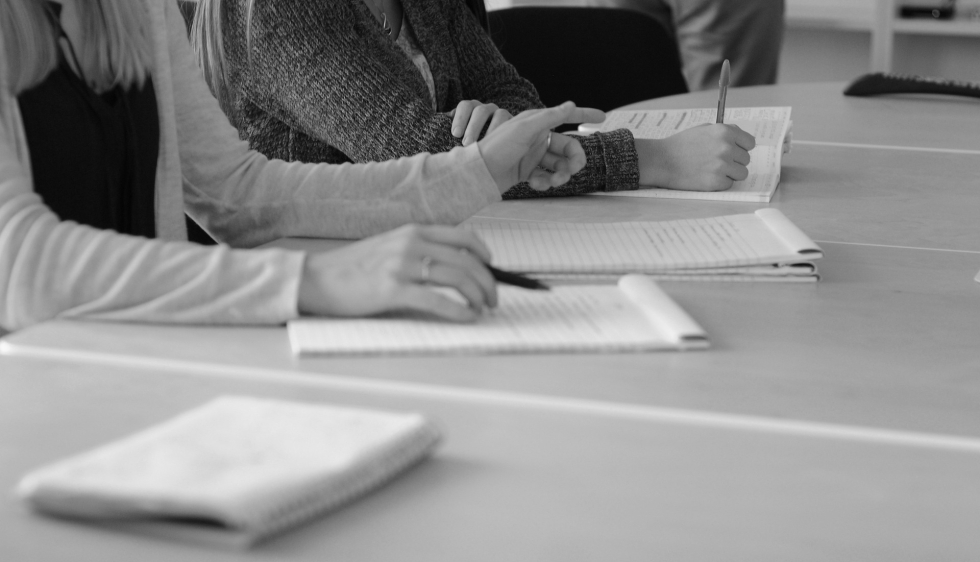 photo en noir et blanc de personnes en réunion, écrivant sur un cahier